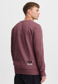 Bordeaux sweatshirt lavet af blødt stof, med rund hals, lange ærmer, lomme på ryggen og sort logo-detalje på den nederste kant.