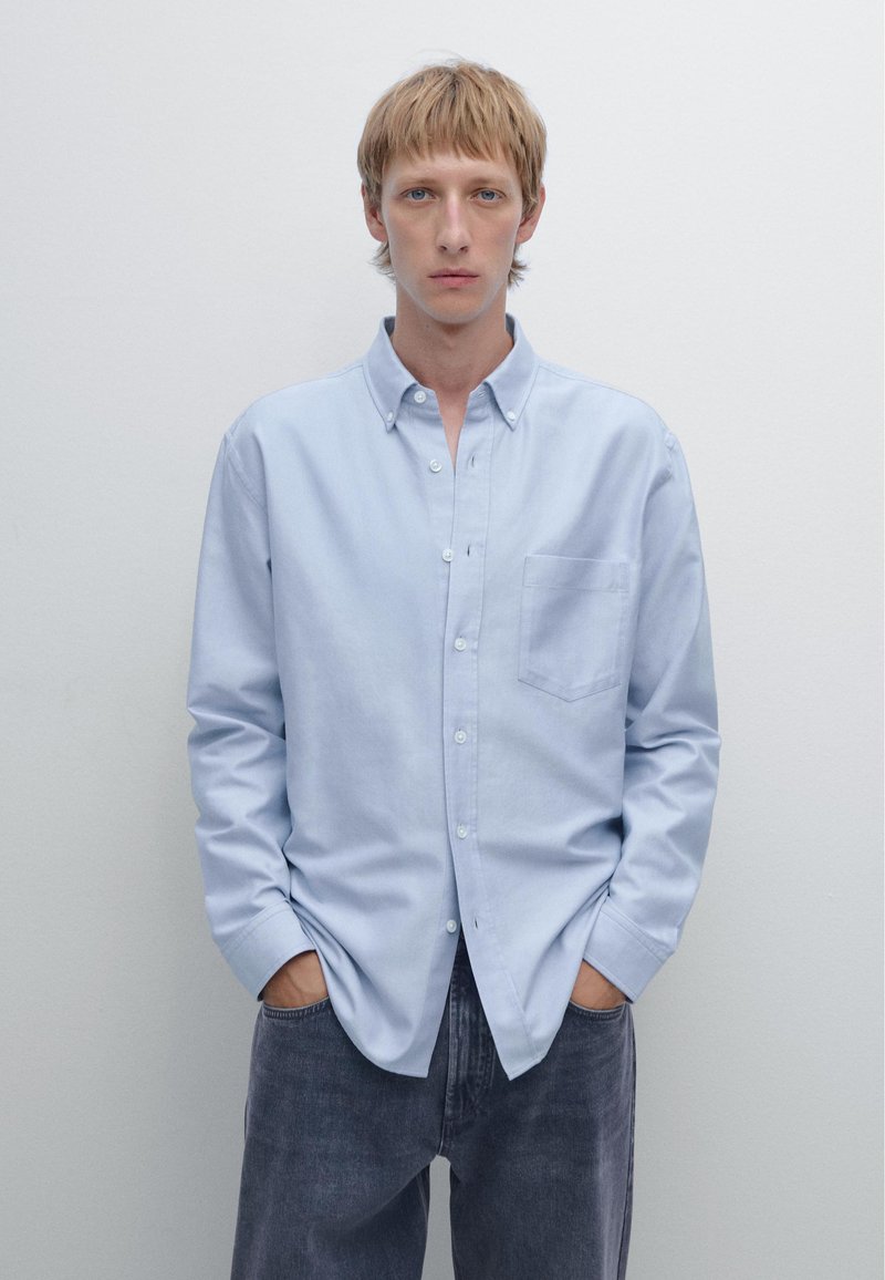 Light blue button-up shirt made of cotton with a chest pocket, long sleeves, and a classic collar, paired with dark gray denim pants.