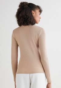 Beżowa bluzka z długim rękawem wykonana z prążkowanego materiału. Posiada okrągły dekolt oraz dopasowany krój, z fakturowanymi detalami na plecach.