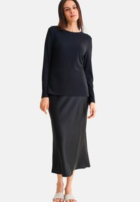 Haut noir à rayures côtelées à manches longues associé à une jupe maxi noire lisse. La tenue présente une coupe décontractée et un design minimaliste avec une fente sur le côté.