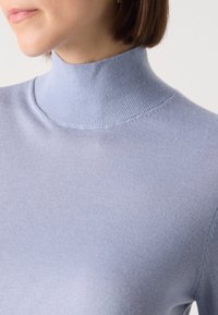 Light blue ribbed turtleneck sweater made from soft fabric, featuring a fitted design and seamless neckline for a sleek appearance.