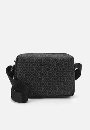 Black rectangular crossbody bag with repeating "CK" pattern and adjustable strap, featuring Calvin Klein logo on front.