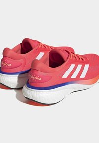 Zapatillas deportivas rojas con rayas blancas, parte superior de malla texturizada, suela acolchada y un talón en contraste con la marca "SUPERNOVA".