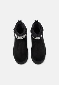 Para czarnych zimowych butów wsuwanych z polarem i białym napisem wokół kołnierza kostki na białym tle.