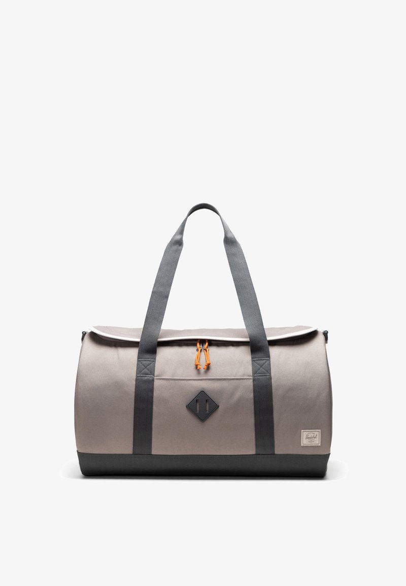 Vaalea harmaa kangaskassi tummanharmaalla pohjalla, jossa on kaksinkertaiset kahvat, oranssi kiristysnauha ja musta timantinmuotoinen logo-patch.