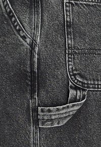 Black denim jeans featuring a side pocket with a stitched seam, subtle texture, and a slightly faded finish.