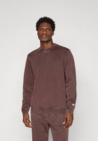 Braunes Fleece-Sweatshirt mit Rundhalsausschnitt und gerippten Bündchen. Verfügt über ein dezentes Logo auf der Brust und eine lockere Passform, kombiniert mit passenden Hosen.