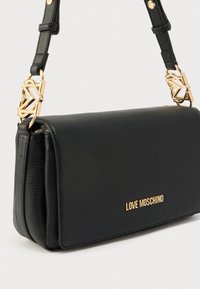 Μαύρη δερμάτινη τσάντα ώμου με υφή, εξαρτήματα σε χρυσό τόνο και χαρακτηριστικό ιμάντα αλυσίδα με διακοσμητικές λεπτομέρειες.