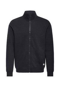 Sweat-shirt noir zippé avec col montant, en tissu doux, doté de poignets côtelés et d'une petite étiquette de marque sur le côté inférieur.
