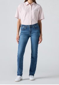 Chemise rose pâle à manches courtes avec boutons, rayée blanche, associée à un jean bleu moyen à jambes droites et des baskets blanches.