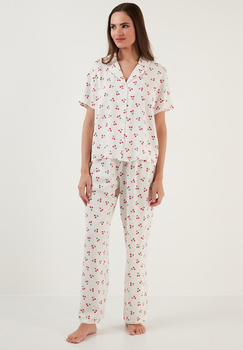 Vitt pyjamasset bestående av kortärmad topp och långa byxor, dekorerat med röda körsbärsmönster på en ljus bakgrund. Slät, avslappnad passform.