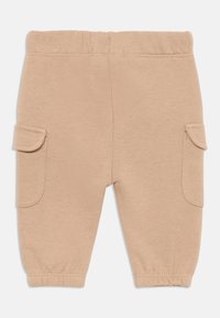 Pantalones de algodón beige con una textura suave, que cuentan con bolsillos laterales y puños elásticos en los tobillos para un ajuste cómodo. Diseño simple y casual.
