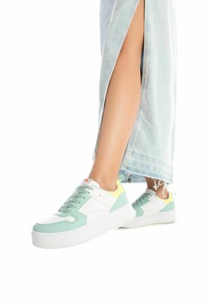 Zapatillas blancas y verde menta con materiales texturizados, suela gruesa blanca y acentos amarillos claros. Los cordones son verdes y presentan un logo.