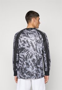 Langärmliges Hemd mit einem schwarz-grauen Camouflage-Muster, rundem Halsausschnitt und kontrastierenden schwarzen Ärmeln. Der Stoff wirkt leicht und glatt.