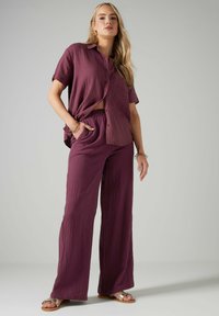 Chemise violette texturée à manches courtes associée à un pantalon ample assorti. Comprend un col, une fermeture à boutons et une taille élastique.