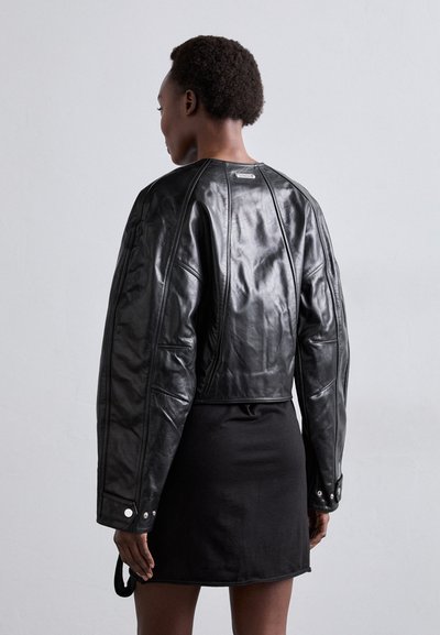 Fekete bőrből készült, rövidített dzseki ejtett vállakkal, sima textúrával, látható varrással és ezüst hardware részletekkel.