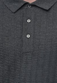 Camisa polo de malha cinza escura com textura ribete vertical e três botões redondos na pala.