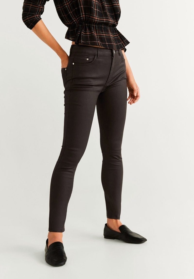 Femme portant un pantalon skinny noir, des chaussures slip-on noires et un haut peplum à carreaux noirs avec des manches courtes.