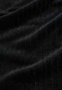 Schwarzer, strukturierter Stoff mit vertikalen Streifen und einer weichen, plüschigen Oberfläche. Das Material scheint ein leicht erhabenes Muster aufzuweisen.