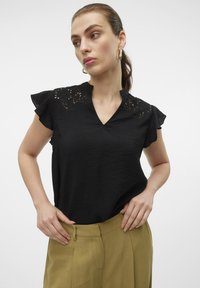 Top nero a maniche corte con scollatura a V, caratterizzato da dettagli in pizzo floreale sulle spalle. Tessuto leggero con superficie testurizzata.