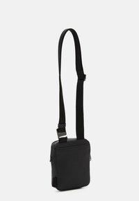 Borsa a tracolla nera in materiale sintetico testurizzato, caratterizzata da una forma quadrata compatta, tracolla regolabile e chiusura con zip.