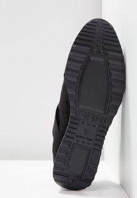 Semelle de chaussure noire avec un motif de bande de roulement profond et le texte « Made in China », affichée sur un fond blanc en coin.