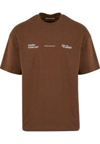 Barna pamut póló rövid ujjakkal, fehér nyomtatott szöveggel: "Another Cotton Lab®," "OFFLINE AZ ÚJ LUXUS," és "Off Season @AnotherCotton."