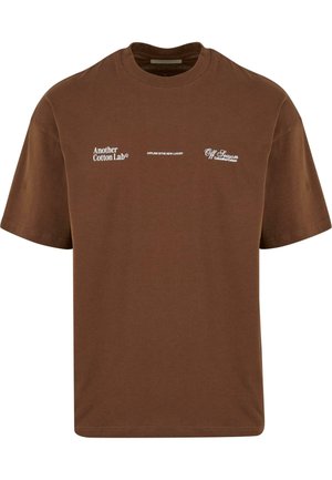 Barna pamut póló rövid ujjakkal, fehér nyomtatott szöveggel: "Another Cotton Lab®," "OFFLINE AZ ÚJ LUXUS," és "Off Season @AnotherCotton."