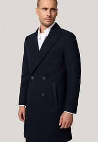 Granatowy wełniany płaszcz dwurzędowy z klapami, bocznymi kieszeniami i zapięciem na dwa guziki. Gładka tekstura i dopasowany krój.