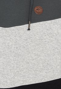 Sudadera gris y negra con una superficie texturizada, que presenta una parte superior gris oscura y un parche de cuero redondo con el logo. Incluye cordones.