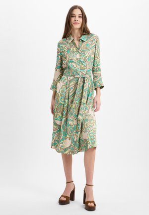 Gekraagde jurk met een paisleypatroon in groen, turquoise en beige. Beschikt over driekwart mouwen, een ceintuur om de taille en een midi-lengte.