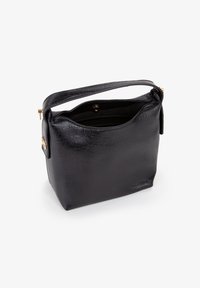 Sort, tekstureret lædertaske med en struktureret form, et enkelt top håndtag og guldfarvet hardware; lukning med lynlås på toppen. Indvendigt synligt.