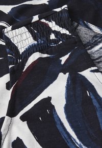 Tessuto navy e bianco con motivi astratti di pennellate in blu e marrone. Presenta una vita elasticizzata con dettagli arricciati.
