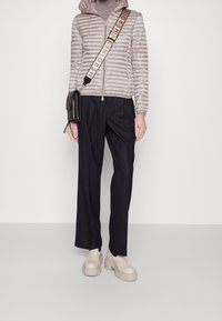 Lichtgrijze pufferjack met horizontale quilting, gestreepte zwarte broek en dikke crèmekleurige plateau-schoenen, geaccessoireerd met een zwarte handtas.