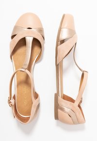 Sandalias planas de cuero y ante beige con correas en los tobillos y puntas descubiertas, mostradas en vistas superior y lateral sobre un fondo blanco.