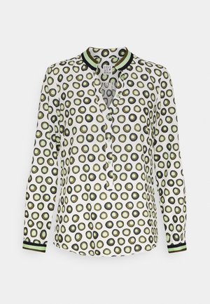 Blouse blanche à manches longues avec motif circulaire vert et noir, boutonnée sur le devant, col et poignets à rayures vertes et noires.