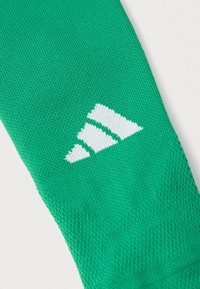 Πράσινο πλεκτό ύφασμα με τρεις λευκές ρίγες διατεταγμένες σε τριγωνικό σχήμα πάνω σε λευκό φόντο.