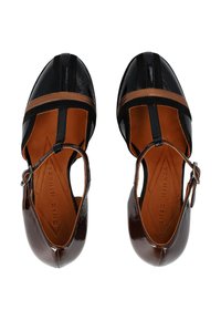 Scarpe in pelle nera e marrone con punta chiusa, lati ritagliati e una cintura. Caratterizzate da motivi geometrici e una texture lucida.