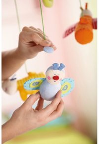 Soft, blue plush butterfly with patterned wings and a round body. Held by a hand, suspended among colorful hanging decorations.