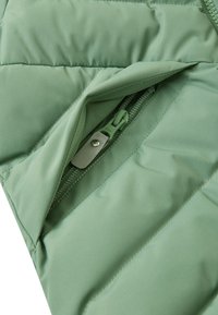 Secțiune dintr-o jachetă verde căptușită cu un buzunar cu fermoar. Textură netedă și detalii de cusătură în diagonală pe țesătură. Fermoarul are un tab metalic.