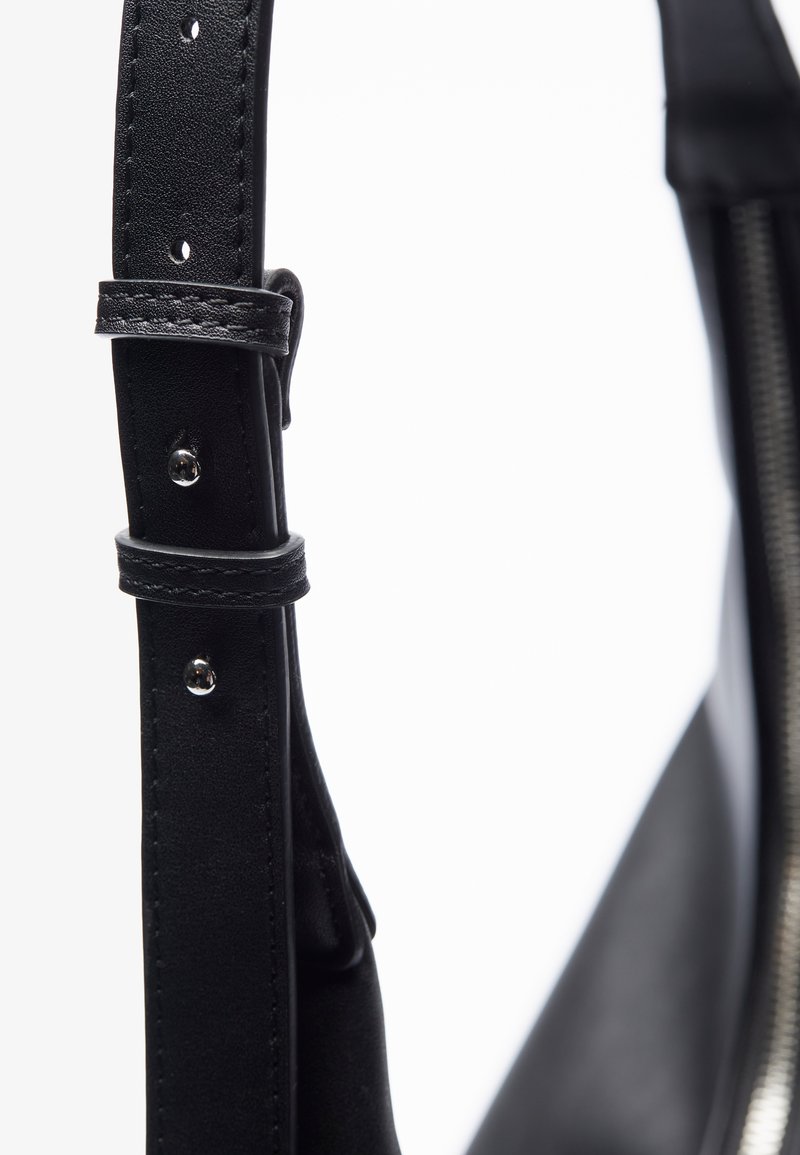 Correa de bolsa de cuero negro con agujeros ajustables, costuras tonales y una textura suave. Presenta un detalle de presión cerca de la hebilla.