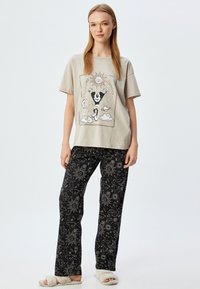 Lichtgrijs katoen t-shirt met een grafisch ontwerp, gecombineerd met zwarte pyjamabroek met witte celestiale patronen. Zacht, comfortabel materiaal.