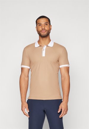 Tan polo shirt with a white collar and sleeve accents, featuring a minimal design and soft texture. Worn with navy pants.