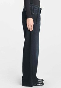 Jeans droits en denim foncé avec une texture lisse, taille haute, cinq poches et passants de ceinture, portés avec des chaussures noires.