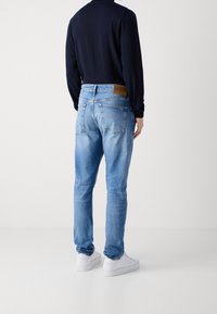 Ljusblå denimjeans med rak passform, med en tan färgad läderetikett i midjan, fyra fickor och en lätt urtvättad textur.