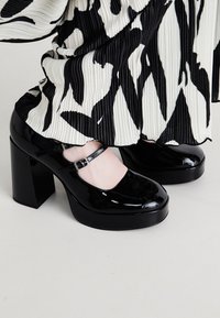 Scarpe con piattaforma in vernice nera, con punta arrotondata e cinturino alla caviglia, caratterizzate da un tacco alto chunky e una finitura lucida e raffinata.