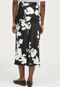 Jupe noire avec un imprimé floral blanc, fabriquée à partir d'un tissu lisse. Mi-longue avec une légère évasement, assortie à des ballerines noires simples.