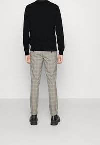 Schwarzer Pullover mit langen Ärmeln, graue karierten Hosen und schwarze Schuhe. Die Hosen haben ein kariertes Muster und einen regulären Schnitt.