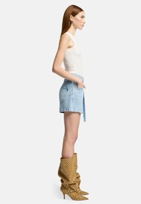 Lichtblauwe denim rok met zakken, gecombineerd met een aansluitend wit top en knielange, slouchy bruine laarzen met witte stippen.