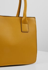 Borsa a mano gialla in pelle con texture liscia, forma rettangolare e manici resistenti. Presenta dettagli di cucitura lungo i bordi. Nessun hardware visibile.
